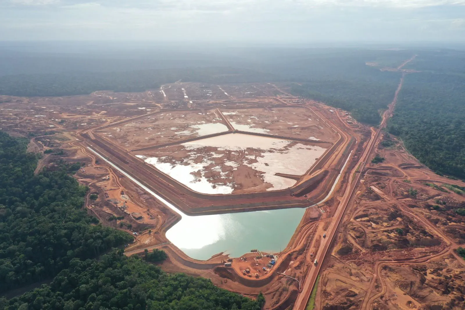 Vista aérea de grande área de reservatório com lagoa esverdeada, cercada por floresta
