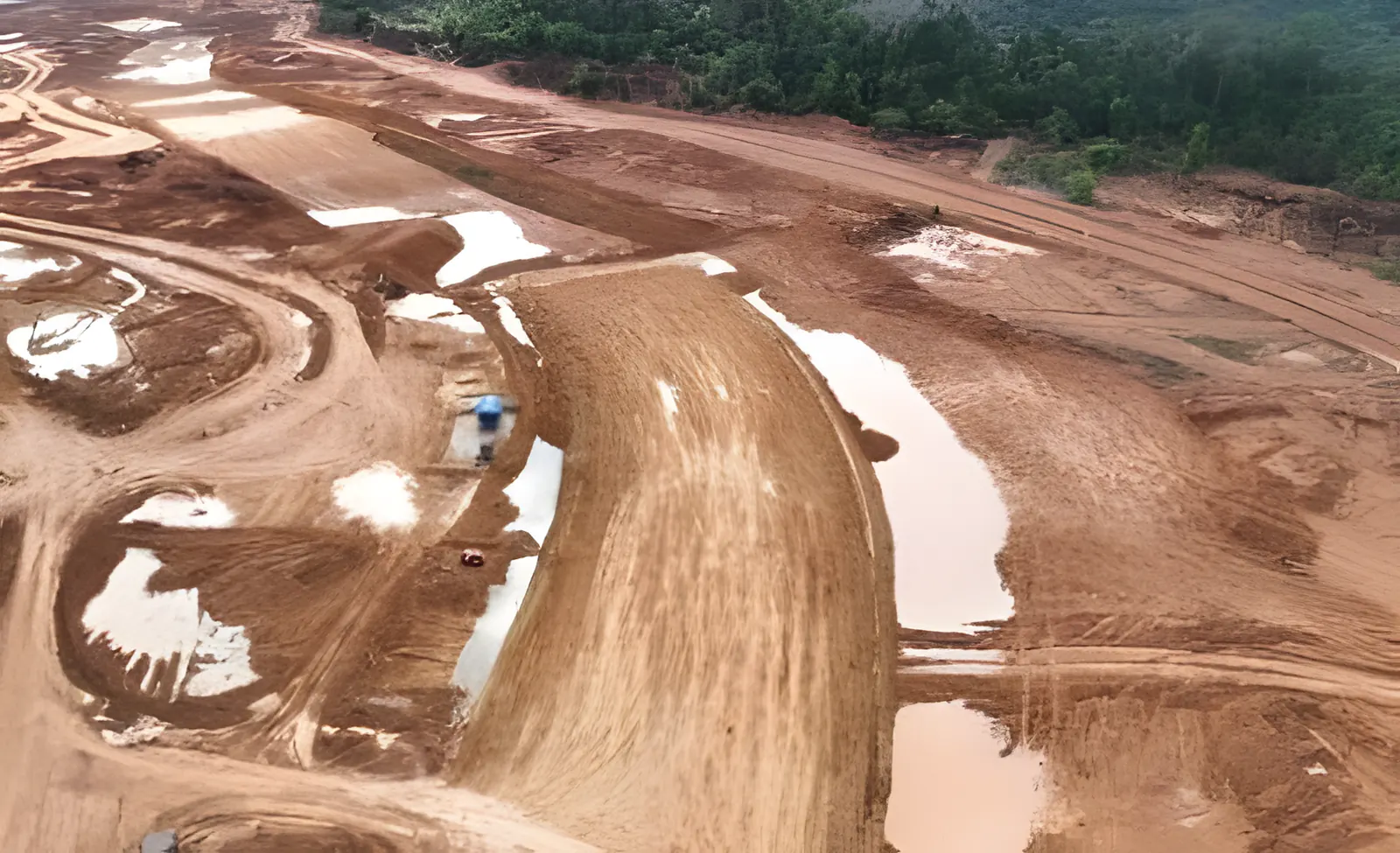 Vista aérea de aterro em curva, com poças d’água e caminhos de serviço em terra vermelha