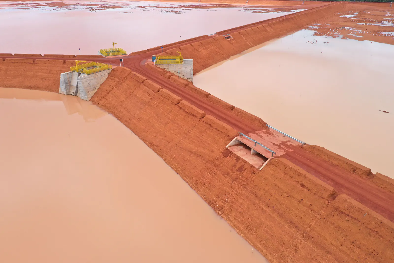Crista da Barragem SP24 entre reservatórios de água avermelhada, com estruturas de concreto