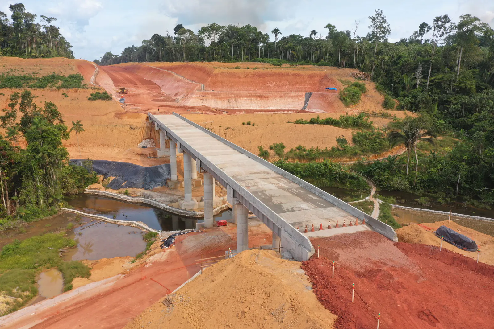 Ponte de concreto sobre curso d’água, com taludes de terra vermelha nas cabeceiras