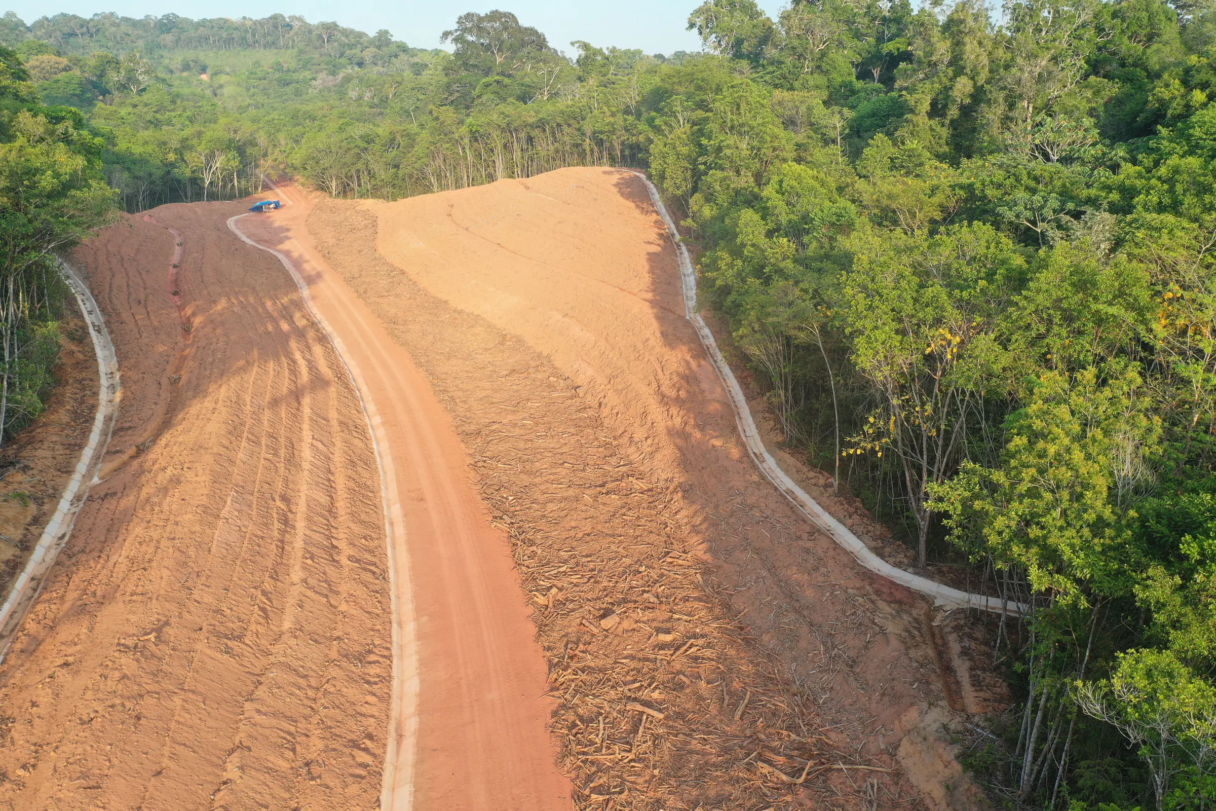 Vista aérea de talude em conformação aberto entre a floresta, com estrada de serviço e canaleta de drenagem na borda