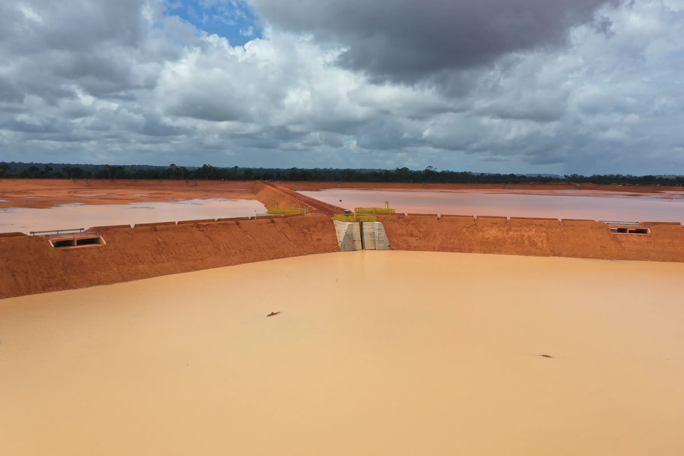 Vertedouro de concreto no reservatório de barragem de rejeito, sob céu nublado